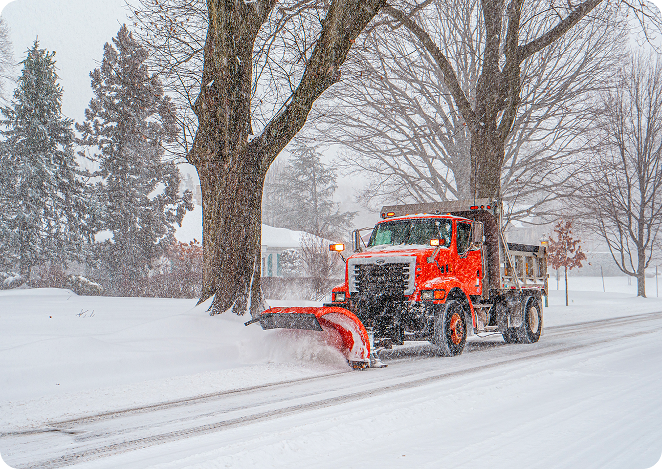 Red snowplow clearing snowy road.